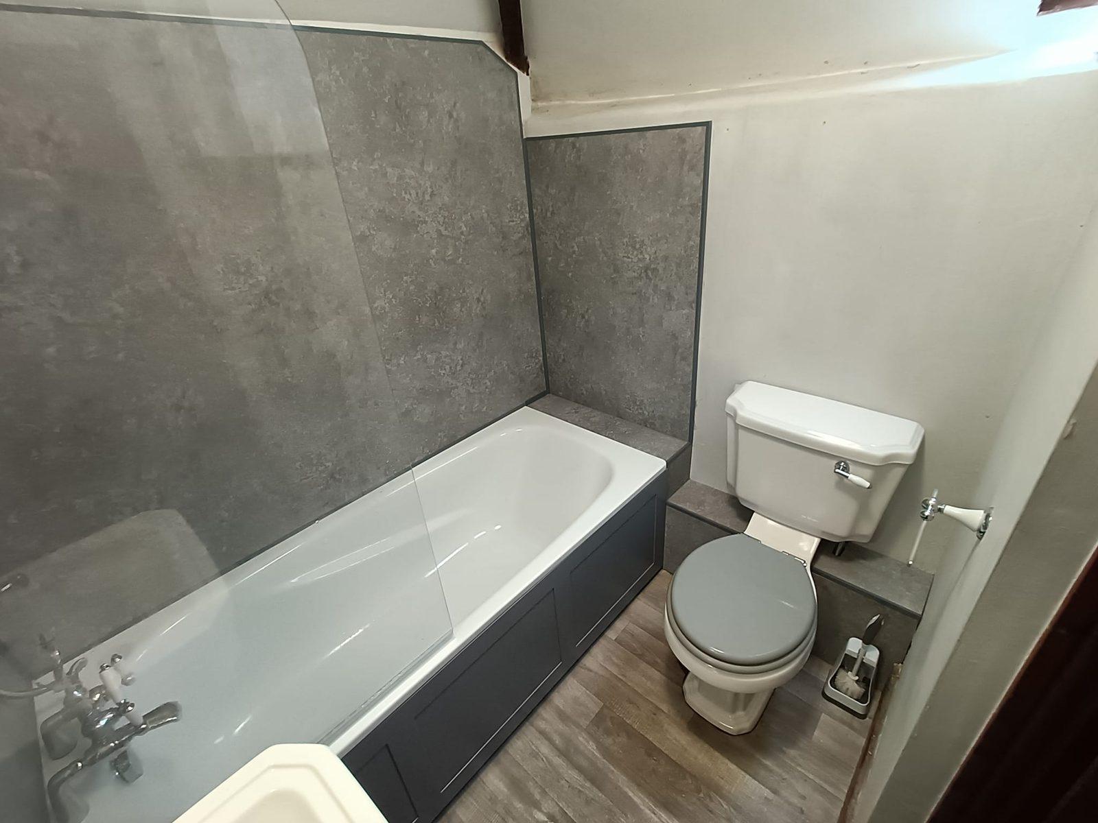 Compact bathroom renovation with grey panelled walls and a navy bath