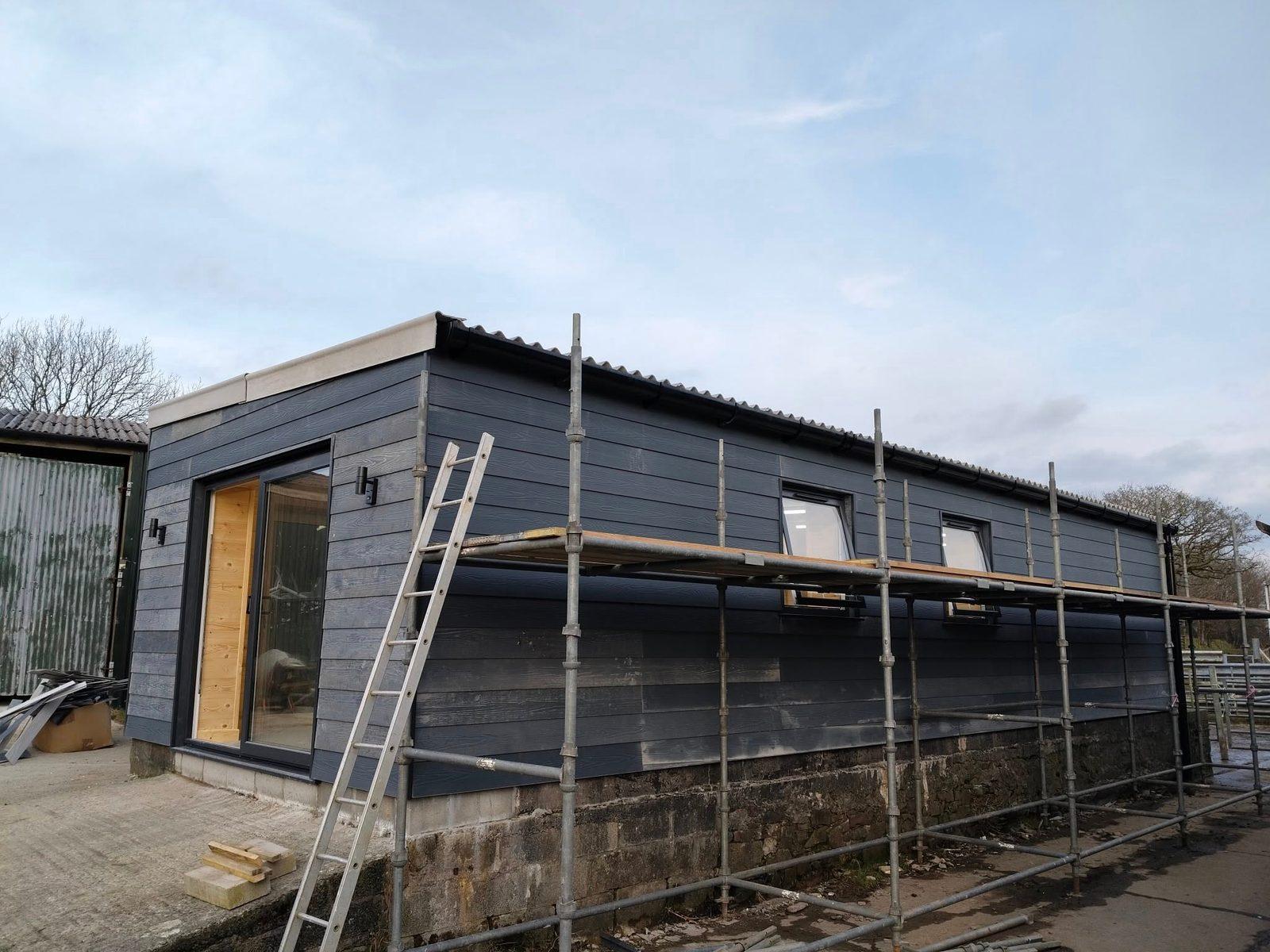 Dark timber-clad new build with sliding doors and scaffolding