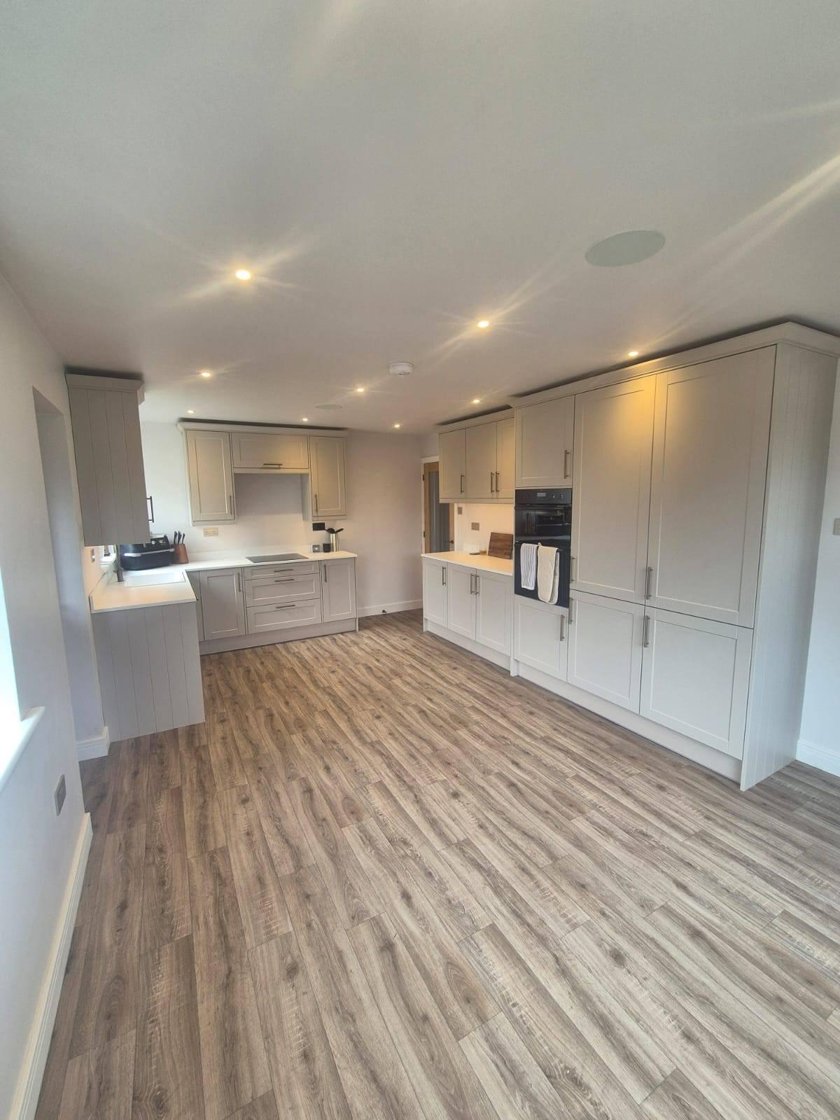 Completed open-plan shaker kitchen with engineered oak flooring and integrated appliances